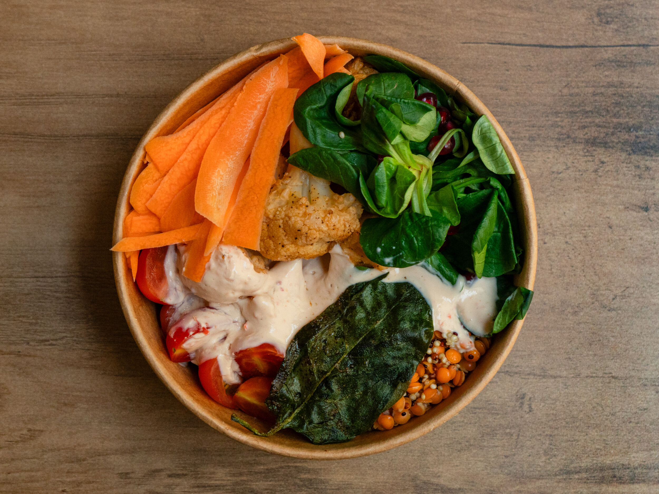 Draufsicht der veganen „Ma'Puaa Bowl“ von Mames Bowls & Wraps Gera: Eine Schale gefüllt mit Quinoa, roten Linsen, Karotten, geröstetem Blumenkohl, Feldsalat, Kichererbsen und einem cremigen Tahini-Dip. Auch glutenfrei erhältlich.