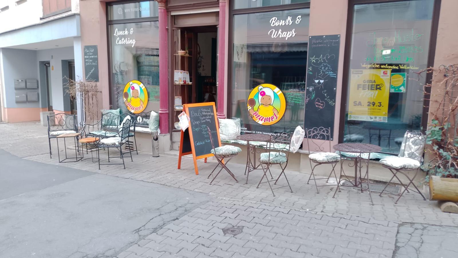 Die Außenansicht des Mames Ladens in Gera, mit dem Logo im Fenster und den gemütlichen Sitzgelegenheiten auf dem Gehweg.