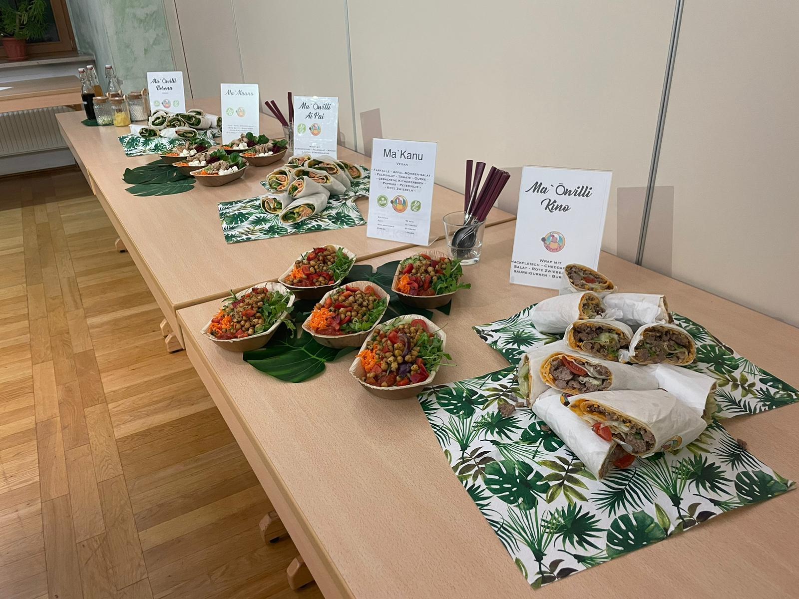 Professionelles Catering-Buffet von Mames Gera, übersichtlich angerichtet mit verschiedenen Bowls (Ma'Kanu) und Wraps (Kino), alle klar beschriftet.